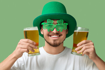 Happy young man in leprechaun's hat with glasses of beer on green background. St. Patrick's Day...