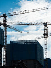 Construction cranes are silhouetted against a bright blue sky, signifying urban development and growth.