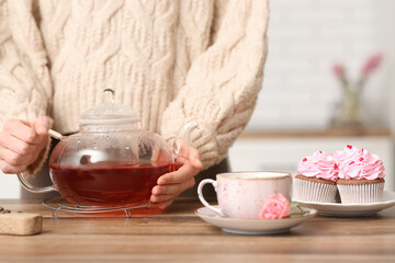 Young woman holding teapot with hibiscus tea in kitchen