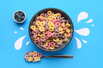 Bowl with colorful sweet cereal rings, blueberries and paper milk drops on blue background