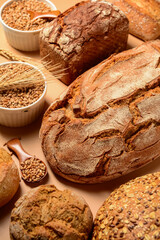 Loaves of fresh bread with buns and wheat spikelets on beige background