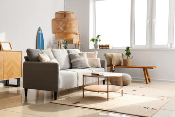 Stylish interior of light living room with comfortable sofa, table, carpet and lamp