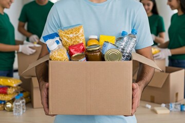 A volunteer holds a box full of donated food items, ready for distribution. This image represents charity, community support, food bank, donation, and helping those in need.