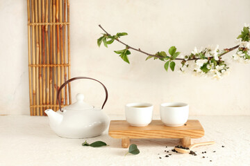 Wooden stand with teapot, cups, spoon of dry tea and leaves on light background