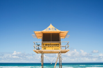 A bright yellow lifeguard tower stands prominently against a clear blue sky, overlooking a tranquil expanse of ocean, Gold Coast, Queensland © pauline.mongarny