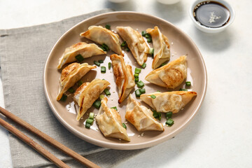 Plate with fried Japanese gyoza, cut green onion and bowl of soy sauce on white background