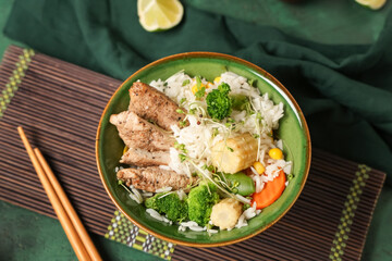 Bowl of tasty rice with chicken and vegetables on color table