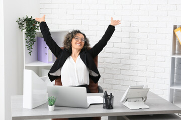 Happy mature businesswoman in eyeglasses at workplace in office