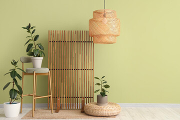 Interior of room with wooden folding screen, chair and houseplants near green wall
