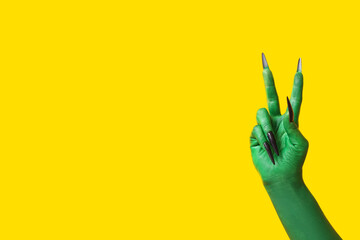Green hand of witch showing victory gesture on yellow background. Halloween celebration