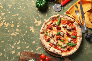 Wooden board of tasty pizza with mushrooms and pumpkin for Halloween celebration on green background