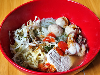 Bakso. The meatballs are served in a red bowl, containing meatballs, pieces of beef bone, yellow vermicelli noodles, vegetables, etc. Looks very delicious and delicious.