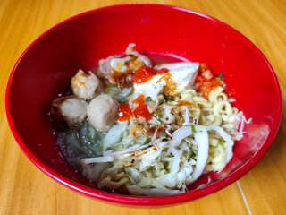 Bakso. The meatballs are served in a red bowl, containing meatballs, pieces of beef bone, yellow vermicelli noodles, vegetables, etc. Looks very delicious and delicious.