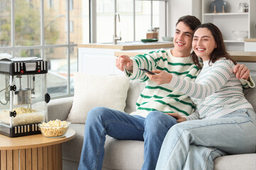 Fototapeta premium Cute couple with modern popcorn machine watching movie at home