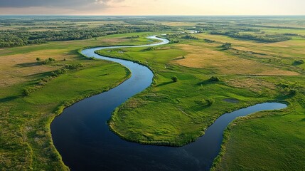 A winding river flowing through vast green fields under a bright sky with distant horizon in a serene natural landscape