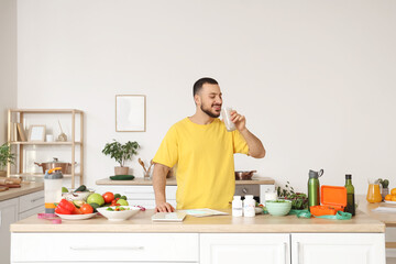 Handsome young man with fresh vegetables drinking healthy smoothie in kitchen. Healthy food concept