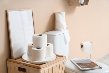 Interior of stylish restroom with toilet bowl, magazine and paper rolls, closeup