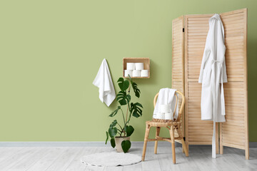 Interior of stylish restroom with chair, folding screen and rolls of toilet paper on shelf