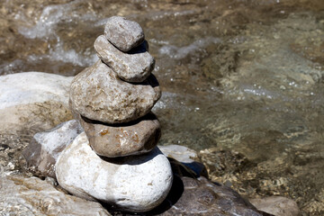 Balancing stones in a serene river setting during a sunny day by the water's edge