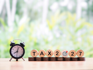 Black alarm clock, Wooden blocks with the word TAX, Number 2025 and stack of coins. The concept...
