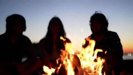 Silhouette of friends gathered around a bonfire at sunset