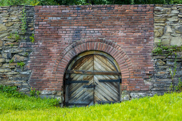Historical wooden gate boarded up with board. Closed double wooden gate in a brick and stone wall