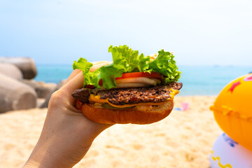 Woman holding burger in a hand against beach background