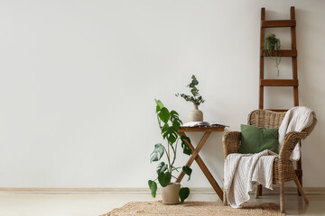 Wicker armchair, ladder and coffee table with houseplants near white wall in room