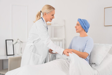 Obraz premium Doctor covering young woman after chemotherapy with blanket in hospital room. Brain cancer concept