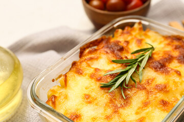 Baking dish with tasty pasta, rosemary and cheese on light background