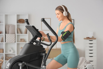Sporty young woman with headphones training on modern exercising bike at home