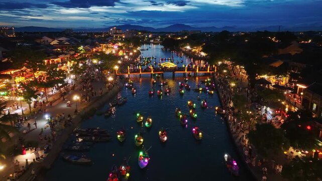 Aerial view of Hoi An city at night in Quang Nam province, Vietnam, a popular tourist destination, with colorful lantern-lit boats sailing along the river.
