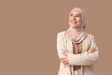 Happy young Muslim businesswoman in hijab on brown background