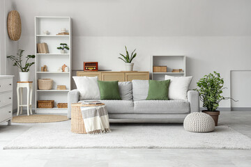 Interior of stylish living room with grey sofa, wicker coffee table and shelving unit
