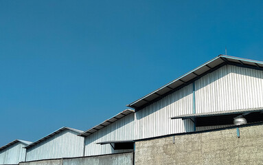 A row of industrial warehouse buildings with metal roofs, captured on a clear sunny day. Suitable for themes of logistics, storage, factory, or industrial zones.