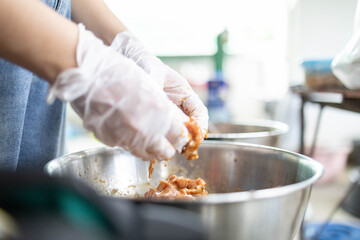 A person is cooking meat in a bowl with gloves on. The person is wearing a blue apron
