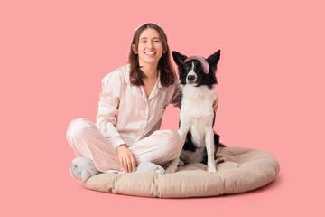Beautiful young woman and cute Border Collie dog in sleep masks sitting on pet bed against pink...