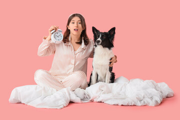 Beautiful young woman and cute dog in sleep masks sitting on bed against pink background