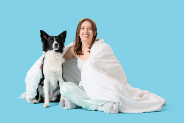 Beautiful young woman and cute Border Collie dog with sleep mask and blanket on blue background