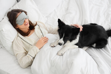 Beautiful young woman with sleep mask and cute Border Collie dog sleeping in bed