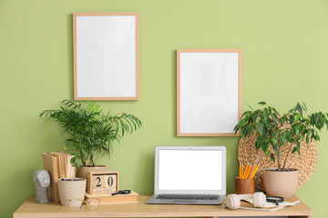 Obraz premium Comfortable workspace with modern laptop, headphones and houseplants near green wall