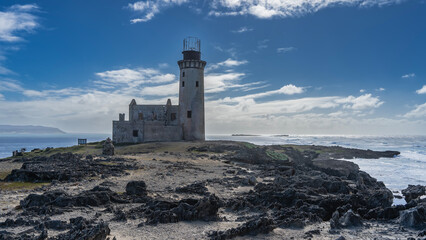 An old lighthouse on a background of blue sky and clouds. A dilapidated building with a tall...