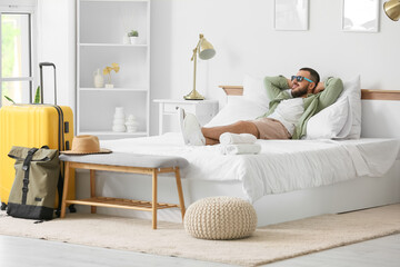 Male tourist with sunglasses lying on bed in hotel room