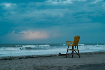 Lone lifeguard chair stands on a sandy beach at dusk overlooking the ocean