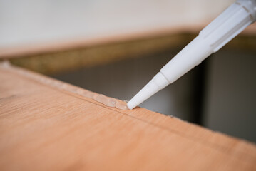 Construction worker is applying silicone sealant with a caulking gun on a wooden surface, ensuring a waterproof and airtight seal during a kitchen sink installation