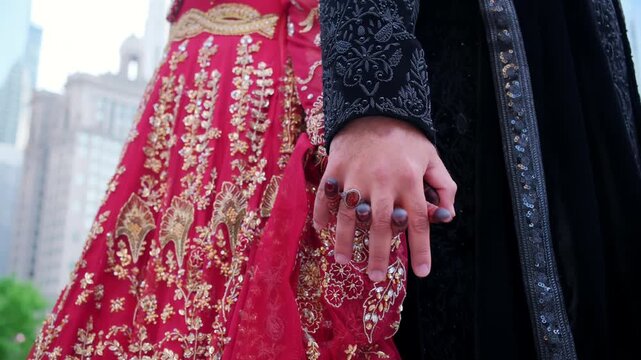Groom is holding brides hands in Traditional henna painting in downtown of the big city. Red color is the traditional Indian clothes, Elements of hindu wedding. 