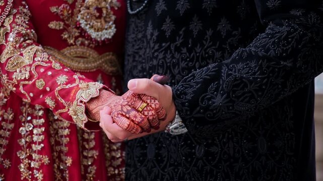 Groom is holding brides hands in Traditional henna painting posing for photo. Red color is the traditional Indian clothes, Elements of hindu wedding. 