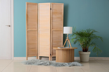 Interior of stylish living room with basket, folding screen and palm tree