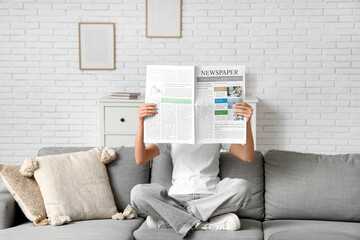 Young woman reading newspaper on sofa at home