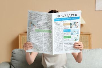 Naklejka premium Young woman reading newspaper on sofa at home